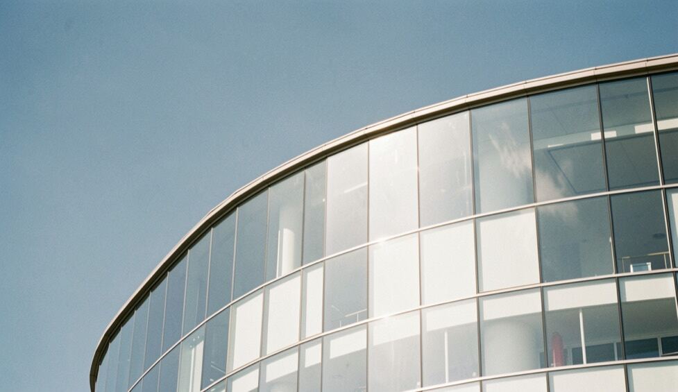 Fachada curva de vidrio blanco bajo un cielo azul claro, con reflejos suaves y líneas arquitectónicas limpias en un día despejado.