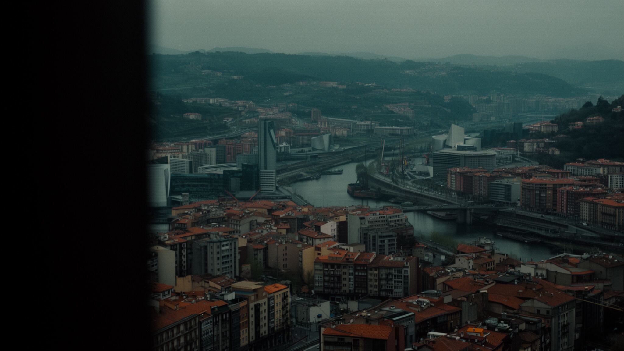 Vista nocturna del río Nervión en Bilbao con reflejos cálidos sobre el agua, edificios de cristal iluminados y una silueta urbana densa al fondo.